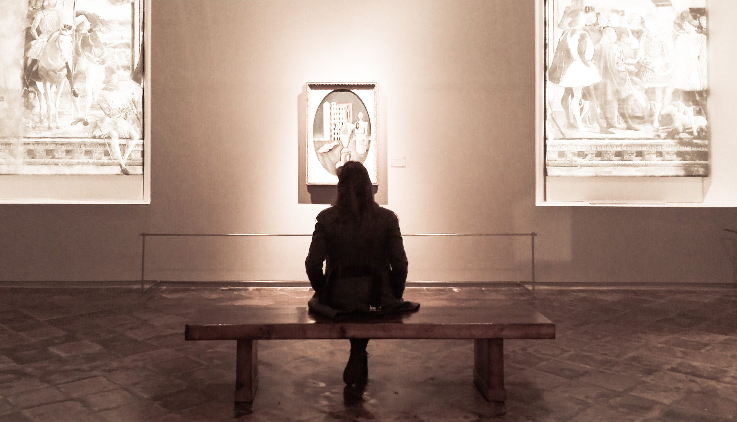 Monica fotografata di spalle, seduta ad ammirare opere d'arte all'interno di un museo